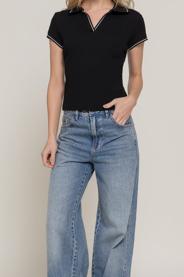 Woman wearing a black top and blue jeans against a plain background